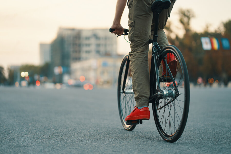 Closeup of casual man legs riding classic bike on city gray road wearing red sneakers and comfy pants. Copy space