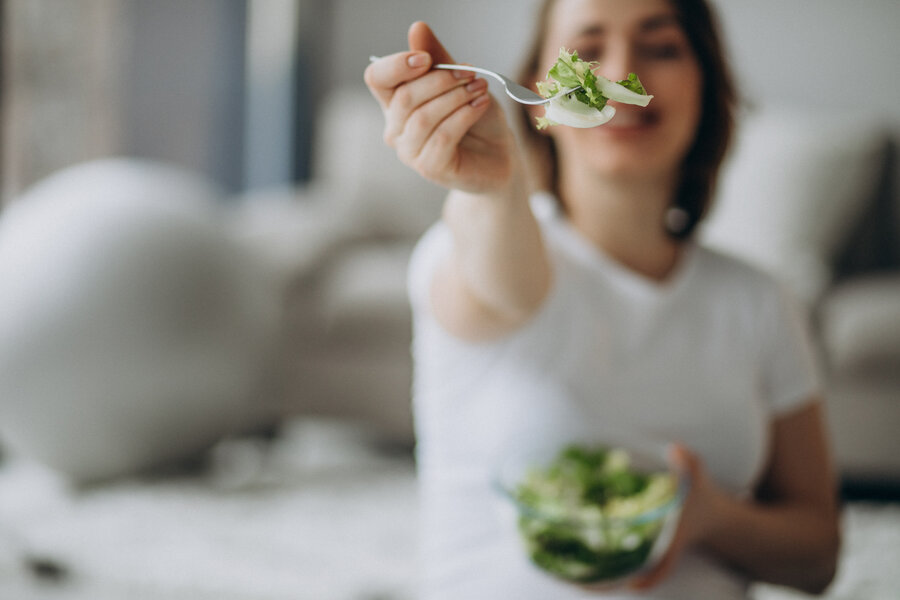Young pregnant woman eating salad at home
