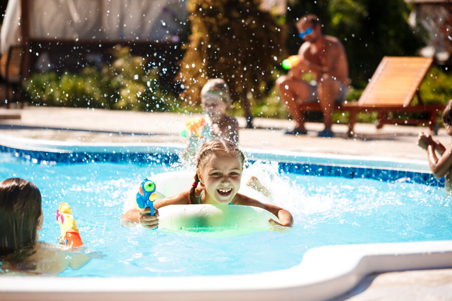 Cheerful children playing waterguns, rejoicing, jumping, swimming in pool. Copy space