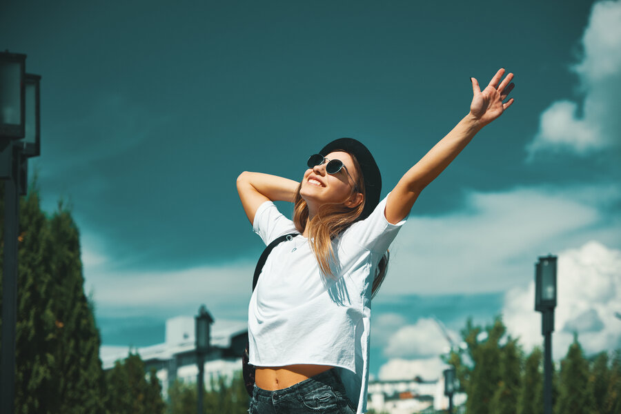 Freedom young woman carefree and happy with open arms on blue sky with hypnotizing sky in background. Caucasian girl in white shirt and jeans, feeling happiness enjoying her travel vacation