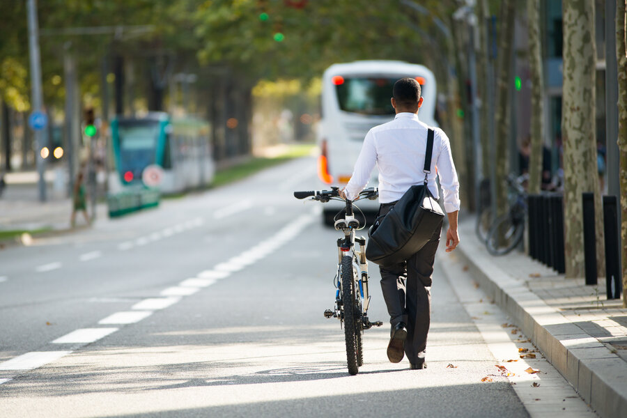 Back view of businessman walking with shoulder bag and bike in street. Young male office employee going after work. Lifestyle concept