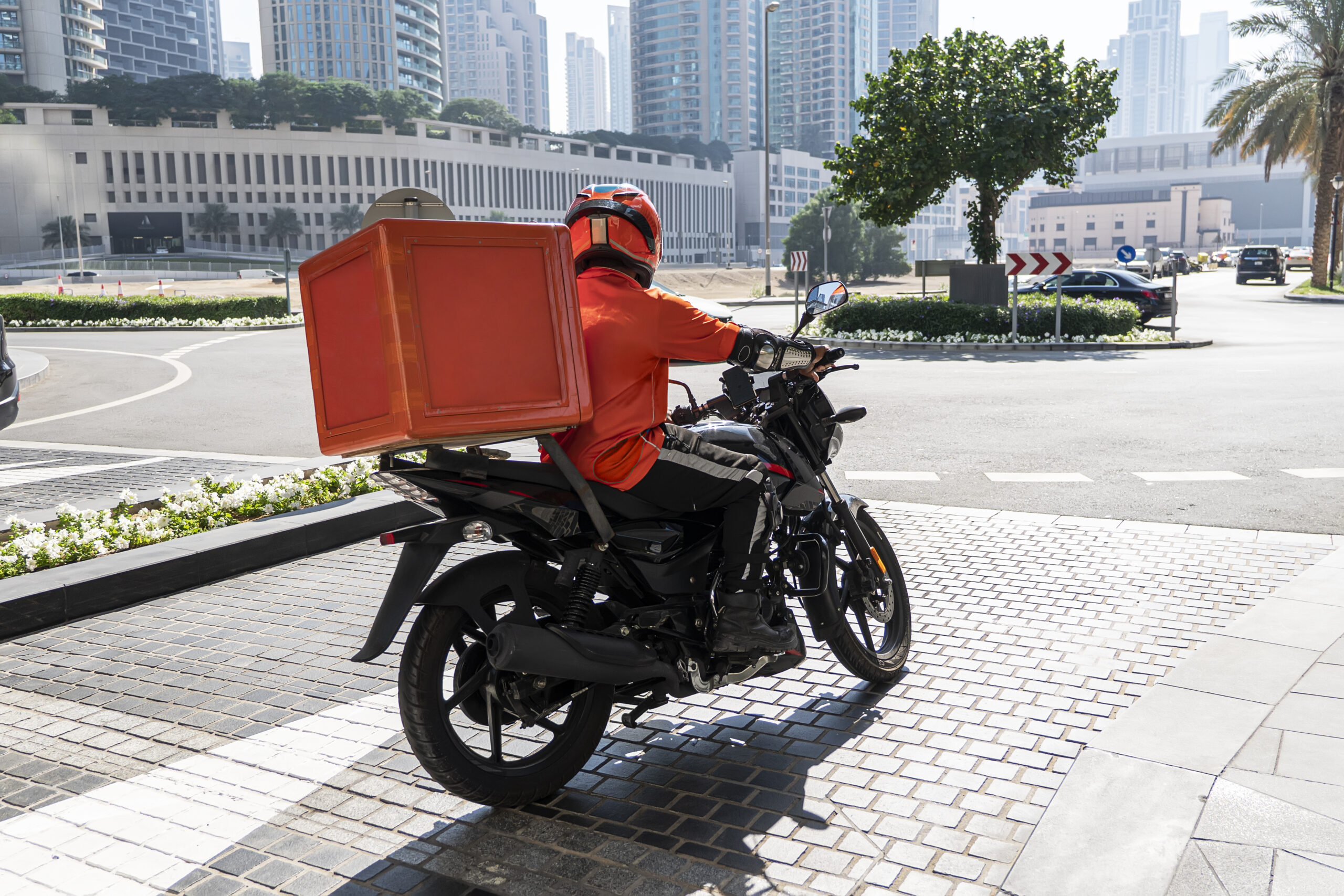 A food delivery courier is driving an order to a customer's home on a moped. takeaway food during quarantine. transport delivery of parcels at home. motorcycle rider with big backpack